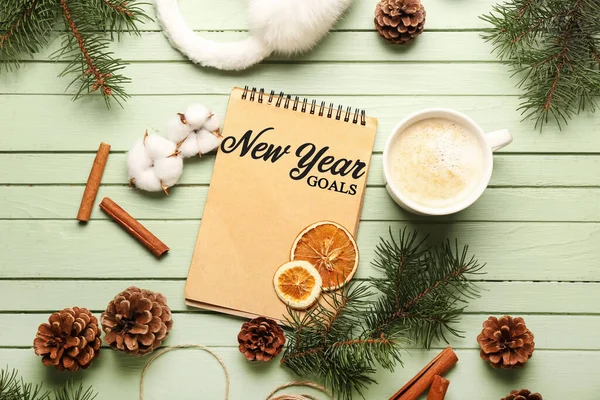 Christmas composition with empty to-do list in notebook, cup of cacao drink and decorations on green wooden background. Concept of new year goals