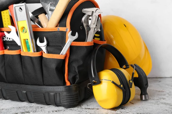 Bag with builder's tools and hearing protectors on light background