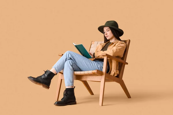 在米色背景的扶手椅上看书的年轻女人 — 图库照片