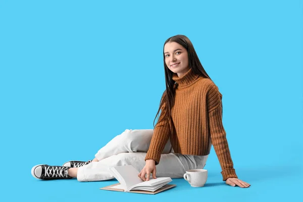 Young Woman Brown Sweater Cup Cocoa Book Sitting Blue Background — Stock Photo, Image