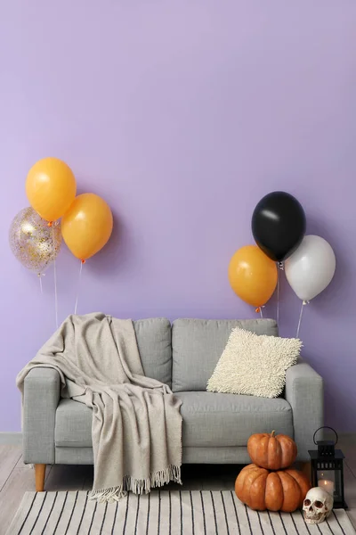 Sofa with Halloween balloons, pumpkins and skull near violet wall