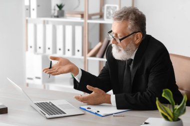 Ofisteki masada dizüstü bilgisayarda görüntülü sohbet eden erkek psikolog.
