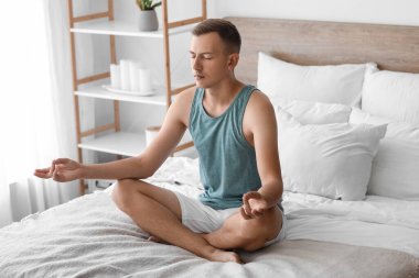 Genç adam evde yatakta meditasyon yapıyor.