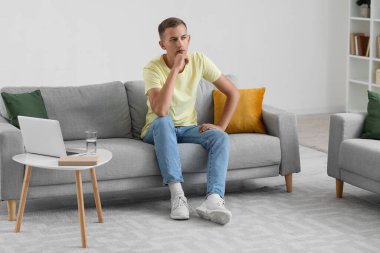 Evdeki kanepede oturan düşünceli genç adam.