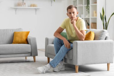 Evdeki kanepede oturan düşünceli genç adam.