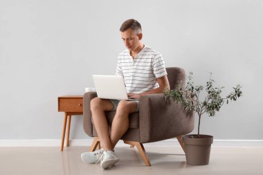 Genç adam hafif duvarın yanındaki koltukta dizüstü bilgisayar kullanıyor.