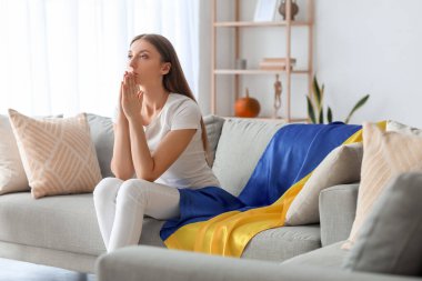 Ukrayna bayrağıyla evde dua eden genç bir kadın.