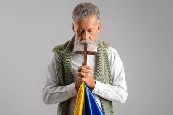 Ώριμος Άνθρωπος Σταυρό Και Σημαία Της Ουκρανίας Προσεύχεται Γκρι Φόντο — Φωτογραφία Αρχείου