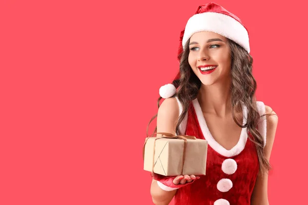 美しいです女性でサンタ衣装とともにクリスマスギフト上の赤い背景 — ストック写真