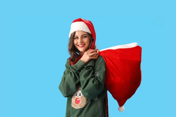 戴着圣诞礼帽的漂亮姑娘拿着蓝色背景的礼品袋 — 图库照片