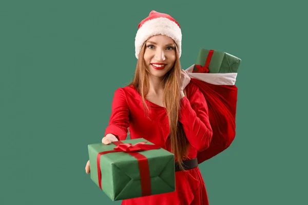 戴着圣诞礼帽 头戴绿色背景礼品袋的年轻漂亮女子 — 图库照片