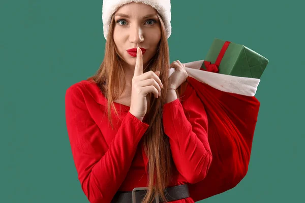 戴着圣诞礼帽 头戴绿色背景的年轻貌美的女人 脸上挂着沉默的表情 — 图库照片