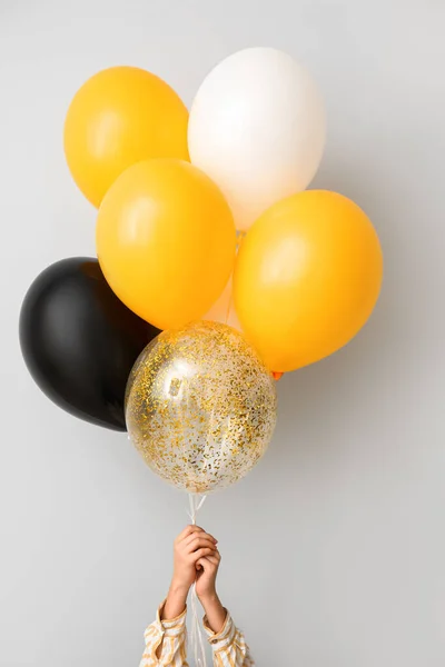 Woman with Halloween balloons near light wall