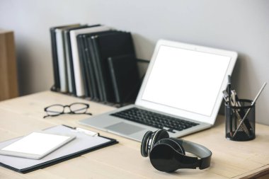 Diz üstü bilgisayar, kulaklık ve tablet bilgisayar beyaz duvarın yanında duruyor.