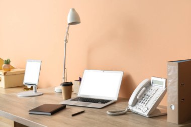 Laptop, kağıt bardak kahve, lamba, tablet bilgisayar, not defteri ve sabit telefon ayakta duran masada.