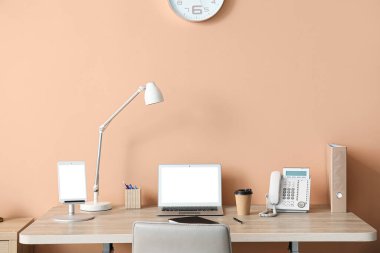 Laptop, tablet bilgisayar, lamba, kahve fincanı ve telefon renkli duvarın yanında duruyor.