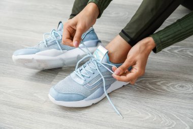 Genç bir kadın ayakkabı bağcıklarını açık tahta zemine bağlıyor.