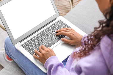 Evdeki kanepede dizüstü bilgisayar kullanan genç bir kadın.