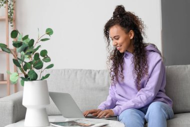 Genç Afro-Amerikalı kadın evdeki kanepede dizüstü bilgisayar kullanıyor.