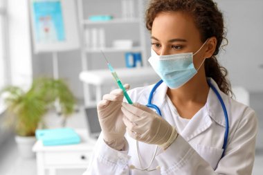 Klinikte tıbbi maskeli ve şırıngalı bir kadın doktor var.