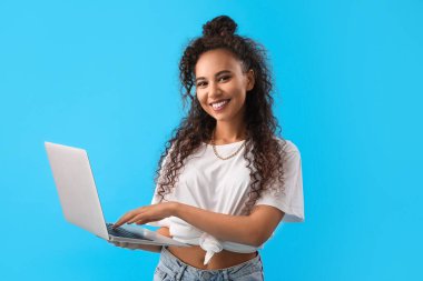 Mavi arka planda dizüstü bilgisayar kullanan genç bir Afro-Amerikalı kadın.