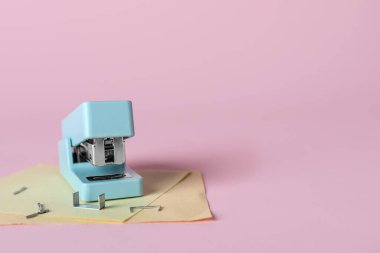 Stapler with sticky notes and staples on pink background