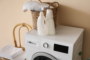 Çamaşır sepeti ve deterjan şişeleri bej duvarın yanındaki çamaşır makinesinde.