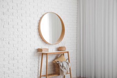 Kitaplı, sepetli ve aynalı bir masa. Odadaki beyaz tuğla duvarda asılı.