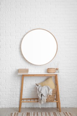 Beyaz tuğla duvarda kitap, sepet ve ayna asılı bir masa.