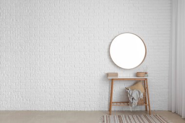 Kitaplı, sepetli ve aynalı bir masa. Odadaki beyaz tuğla duvarda asılı.