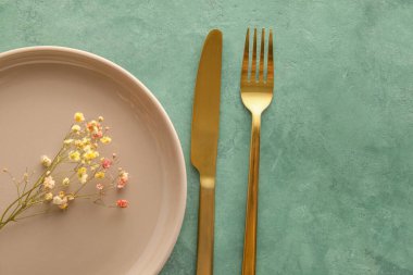 Tabak, çatal bıçak takımı ve yeşil arka planda çiçek dekoru olan masa ayarları