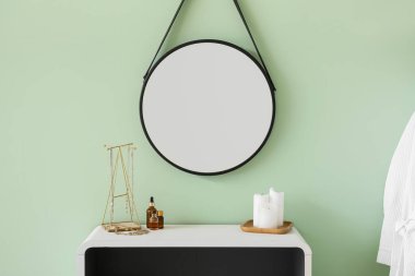 Mumlar, rafta kozmetik ürünleri olan mücevherler ve yeşil duvarın yanındaki ayna.