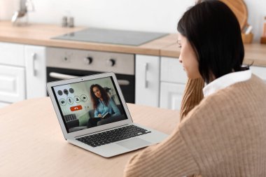 Mutfakta psikologla görüntülü konuşma yapan üzgün genç bir kadın.