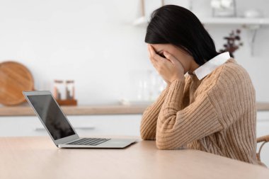 Mutfakta psikologla görüntülü konuşma yapan üzgün genç bir kadın.