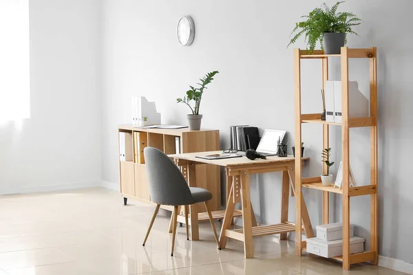 Interior of light room with wooden standing desk and shelf unit near white wall