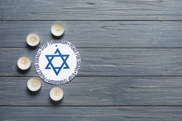 Burning candles, card with text PEACE FOR ISRAEL and STOP TERRORISM on grey wooden background