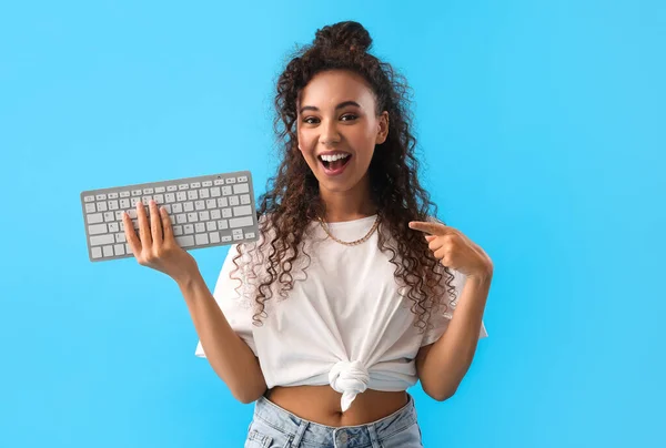 Young African-American woman pointing at computer keyboard on blue background