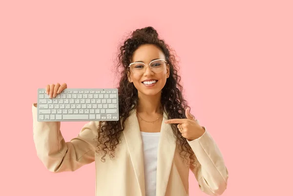 Young African-American woman pointing at computer keyboard on pink background