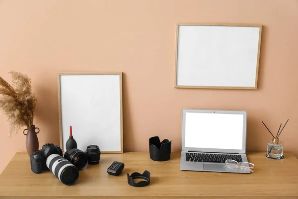 Photographer\'s workplace with laptop, camera, vase and blank frames near beige wall
