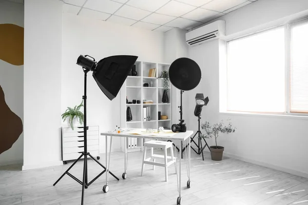 Interior of light office with photographer\'s workplace, shelving unit and equipment
