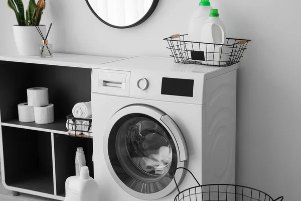 Interior of light laundry room with washing machine, shelving unit and detergent