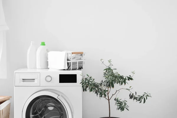 Basket with towels and bottles of detergent on washing machine near light wall