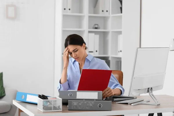 Stressed young businesswoman with folders sitting at table in office