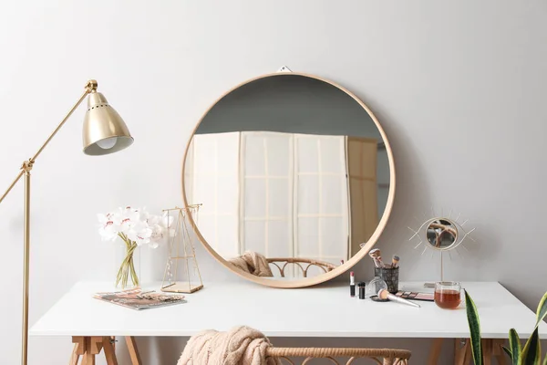 Dressing table with mirrors, flowers in vase, jewelry and cosmetics near light wall