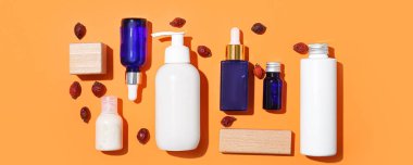 Farklı kozmetik ürünleri ve turuncu arka planda gül böğürtlenleri.