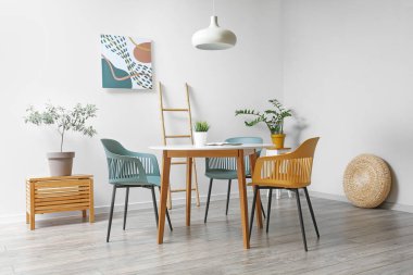 Modern mobilyaları ve beyaz duvarın yanında bitkileri olan şık bir yemek odası.