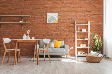 Odanın içinde yemek masası ve tuğla duvarın yanında rahat bir kanepe.