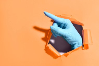 Tıbbi eldiven verin. Renk arkaplanındaki bir delikten bir şeyi işaret ediyor.