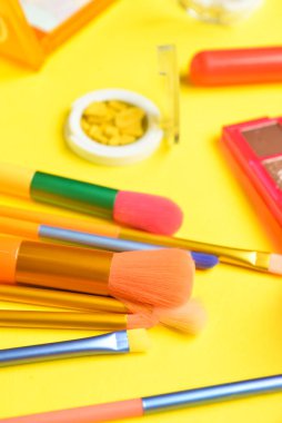 Sarı arka planda makyaj fırçaları ve dekoratif kozmetikler, yakın plan.
