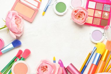 Dekoratif kozmetik ürünlerden, fırçalardan ve açık arkaplanda çiçeklerden yapılmış çerçeve